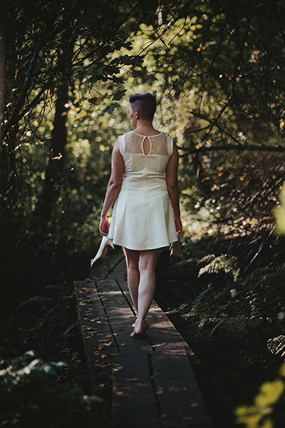 Valkeassa mekossa oleva lyhythiuksinen nainen kävelee pitkospuita pitkin